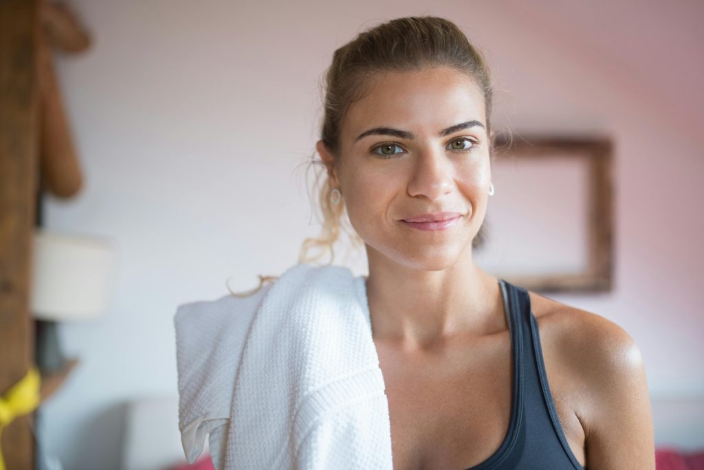 Caucasian woman smiling with a towel after a workout indoors, conveying fitness and positivity.