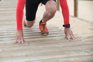 Athlete in red gear gets ready to sprint on a wooden path in sunny outdoor setting.